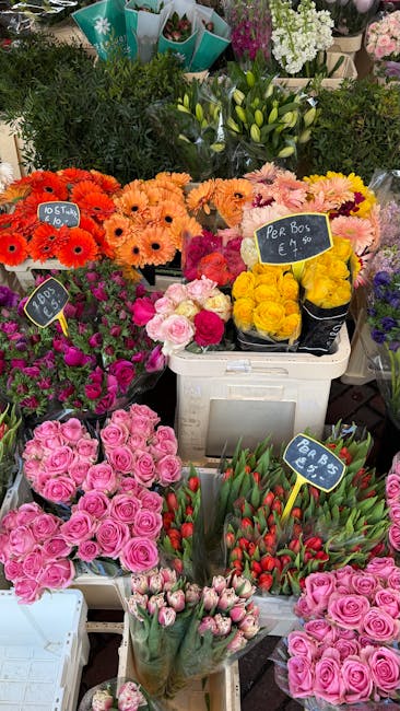 A vibrant display of flower bouquets arranged on a market stall, featuring a variety of fresh flowers including pink roses, red tulips, yellow roses, and orange gerberas, all wrapped in clear cellopha